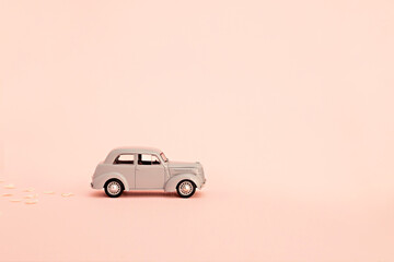 Gray retro toy car delivering flowers and gifts on a pink background. Copy space.