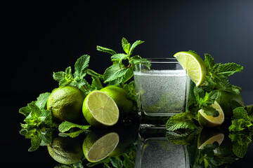 Carbonated drink with limes and mint on a black reflective background.