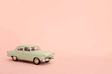 Green retro toy car delivering flowers and gifts on a pink background. Copy space.
