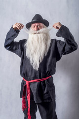 A grey-haired bearded old man, a patriarch in dark national clothes and boots against a light...