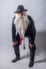 A grey-haired bearded old man, a patriarch in dark national clothes and boots against a light...