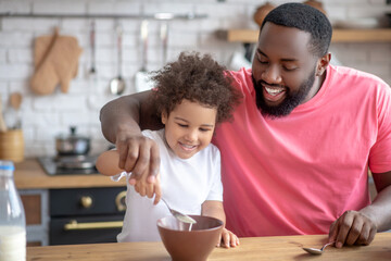 African american bearded man stirring milk in his daughters plate