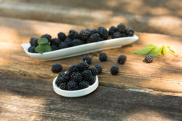Ripe blackberries with leaves in a bowl on a woodenk background