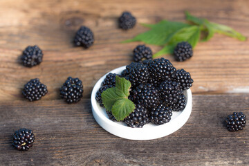 Ripe blackberries with leaves in a bowl on a woodenk background