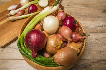  In the frame, onions, leeks, shallots, white, sweet red, yellow onions, green onions. Light wooden background. Close-up..