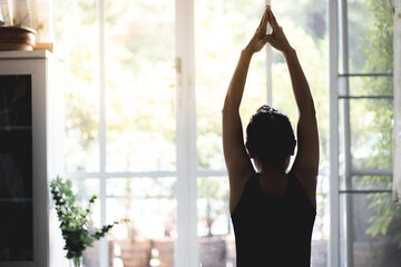 Behind a woman in black is exercising, doing yoga, raising arms, meditating, doing activities at...