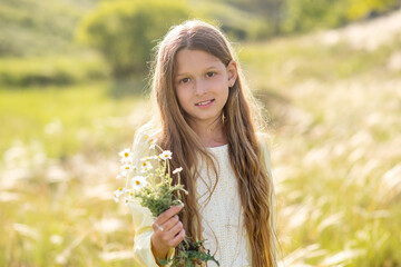 Naklejka na ściany i meble girl in a field. young woman in the field of flowers. Beautiful girl walks in the park. Summer walks and relaxation. Smiling child. Daisies in the hands of a girl