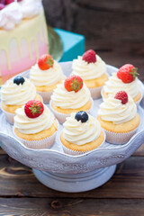 Vanilla cupcakes with cream cheese frosting and fresh berries, blueberry and strawberry. Rustic wooden background.