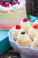 Vanilla cupcakes with cream cheese frosting and fresh berries, blueberry and strawberry. Rustic wooden background.