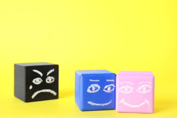 Cubes with drawn faces on yellow background, space for text. Concept of jealousy