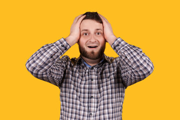 Man with beard holding his head with hand, panic, isolated on orange background.
