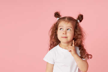 Portrait of surprised cute little toddler girl child over pink background. Looking at camera. Points hands to the left side. Advertising childrens products