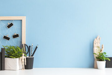 Desk mockup with black and white objects, design boxes, office supplies, books, and plant against blue wall background.	
