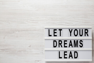 'Let your dreams lead' on a lightbox on a white wooden surface, top view. Flat lay, from above, overhead. Copy space.