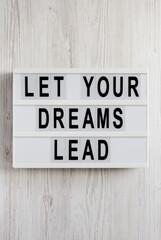 'Let your dreams lead' on a lightbox on a white wooden surface, overhead view. Flat lay, top view, from above.