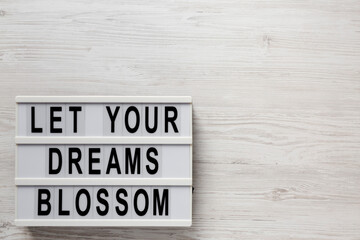'Let your dreams blossom' on a lightbox on a white wooden surface, top view. Copy space.