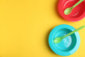 Set of colorful plastic dishware on yellow background, flat lay with space for text. Serving baby food
