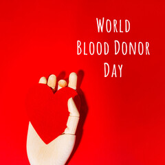 Wooden hand with big red heart in a giving gesture. World Blood Donor Day wording. Donation, help,...
