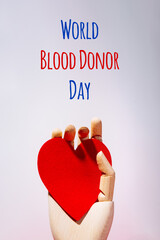 Wooden hand with big red heart in a giving gesture. World Blood Donor Day wording. Donation, help, health issues, antibody plazma concepts. - obrazy, fototapety, plakaty