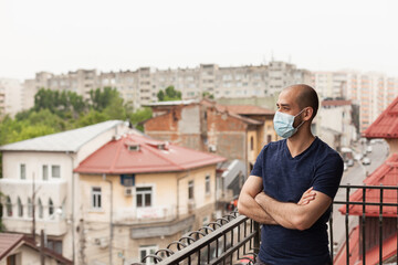 Adult man on balcony wearing face mask during global pandemic.