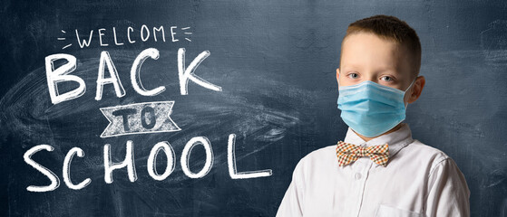 School boy wearing face mask standing against blackboard. Safe back to school during pandemic...