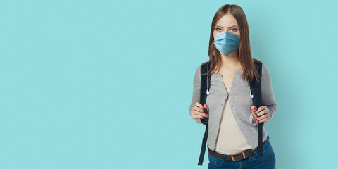 Student woman wearing face mask standing against blue wall with backpack. Safe back to school during pandemic concept. New normal high school education.