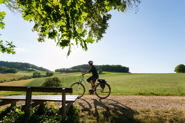 Fahrradtour durch wunderschöne Odenwald Landschaft,
Frau fährt mit Elektro Fahrrad im letzten Sonnen Tageslicht.