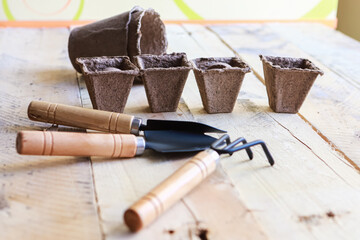 Biodegradeble pots, rake and spade on wooden background. Garden tools.