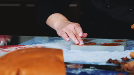 Close-up shot of woman's hands working on gingerbread cookies. In front there is pastry dough.