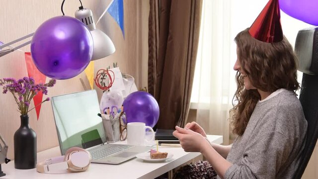 Woman celebrating her birthday through video call virtual party. Lits and blows out candle. Authentic decorated home workplace. Handheld shot with gimbal. Coronavirus outbreak 2020.