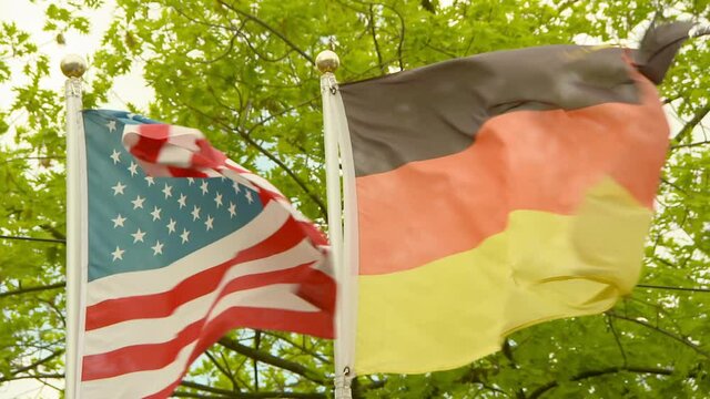 Lockdown time lapse shot of German and American flags waving against trees - Frankfurt, Germany