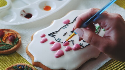 Obraz na płótnie Canvas Royal icing cookie decorating with special food brush and colors. Woman garnishing cookies in different techniques.