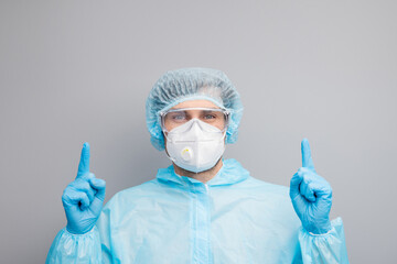 Closeup photo of guy expert doc virology center directing fingers up empty space remind vaccination time wear mask hazmat blue uniform suit protective goggles isolated grey color background