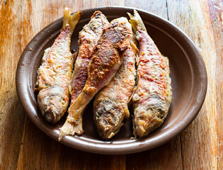 several fried red mullet fishes on ceramic plate on old wooden table at home kitchen