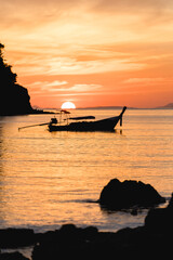 Sonnenuntergang in Thailand mit Longtailboot und Wolken und Felsen im Meer 