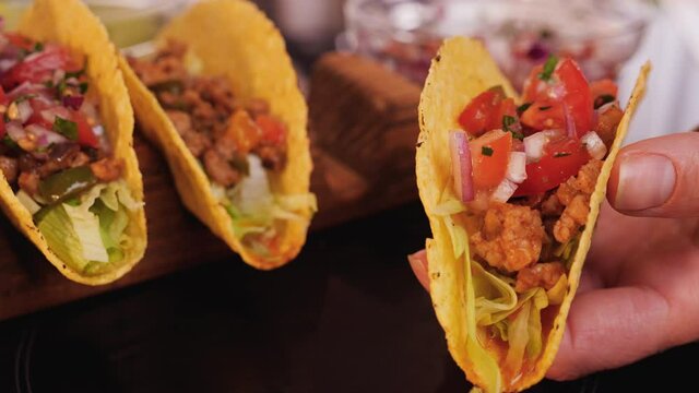 Woman hand stuffing hard taco shells - adding the fresh salsa vegetables mix, holding the shell, camera orbit, close up. Phases of making tacos.