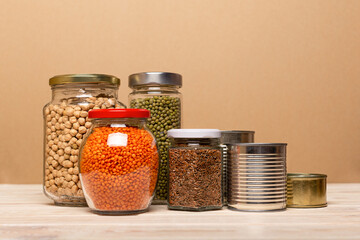 Food ingredients in glass jars and tins on wooden table. Food storage close up