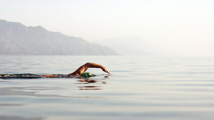 Unknown triathlon swimmer at sea. athletic young woman swimming freestyle in morning open water - Powered by Adobe