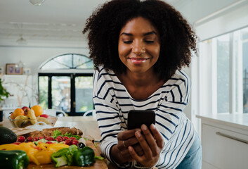 Young female browsing recipes on smartphone and smiling while in the kitchen, portrait