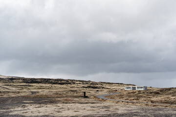 Yellow dry grass to the horizon, a road going into the distance, a lonely house standing on a hill in Iceland.