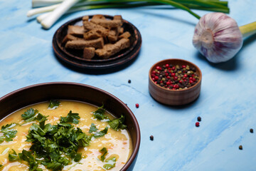 Lentils or pea soup with parsley, onions, garlic, rye bread crackers and aromatic black, red, pink, white pepper set on blue table. Greenery and spices, flavouring, seasoning  concept.