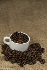 Freshly made coffee in a white cup surrounded by coffee beans on a wooden table. Fresh coffee.