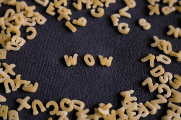 Obraz na płótnie Canvas The word wow written in alphabet pasta in the center surrounded by many mixed letters on a dark background. The element of surprise or excitement concept