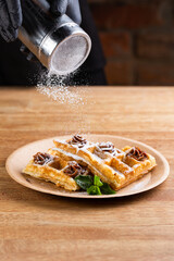 Viennese waffles on a disposable plate with peanut butter, icing sugar and mint. chef decorates dessert with powdered sugar