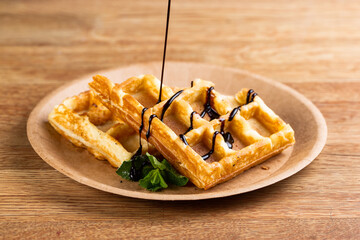 .Viennese waffles on a disposable plate with liquid chocolate, icing sugar and mint. cook pours liquid chocolate for dessert