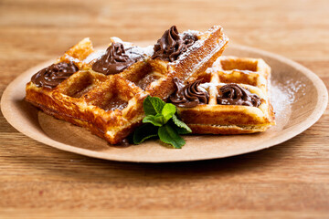 Viennese waffles on a disposable plate with peanut butter, icing sugar and mint.