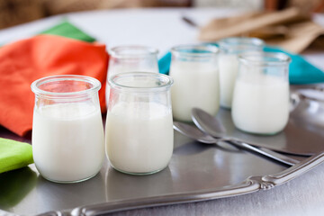 Home made junket in crystal glasses on a metallic tray with spoons and napkins. Top view shot traditional white milk based desserts stills with copy space.