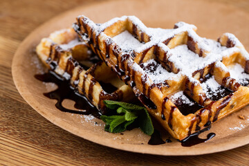 Viennese waffles on a disposable plate with liquid chocolate, icing sugar and mint.
