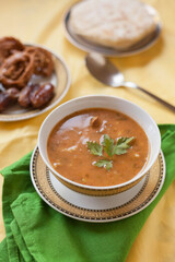 Vertical shot of a bowl of harira, a traditional Moroccan soup dish served hot typical of Ramadan breakfasts accompanied by dates and chebakia sweets on a table set with copy space.