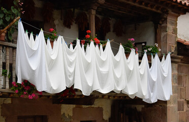 White bed sheets hung up from a balcony or clothes line with clothespin or clothes peg in a rural house made of wood and rock. 
